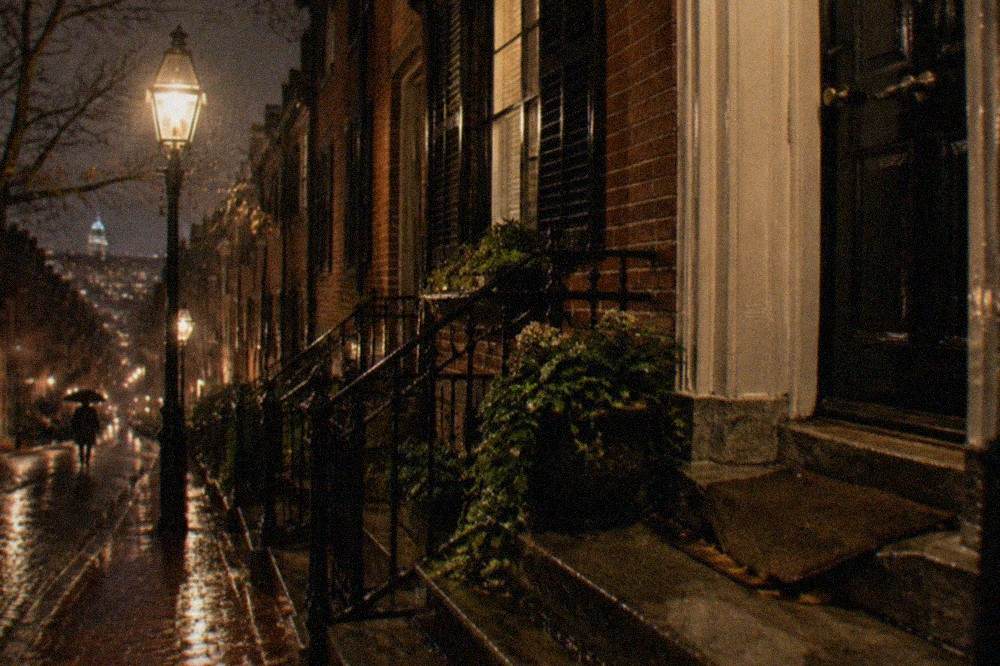 A narrow lamplit Beacon Hill street with brick row houses and iron railings at night