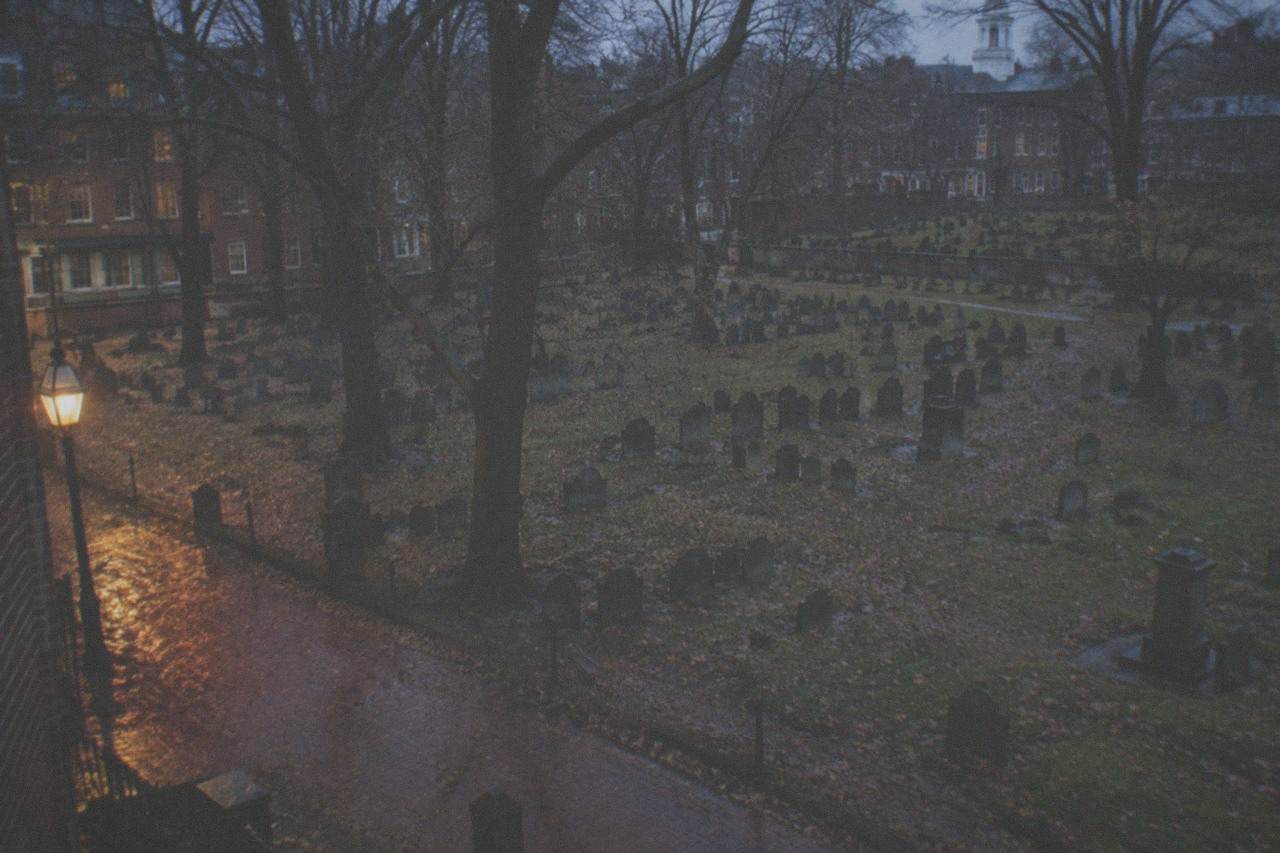 Old slate gravestones tilted among trees at dusk in a colonial burying ground in Boston