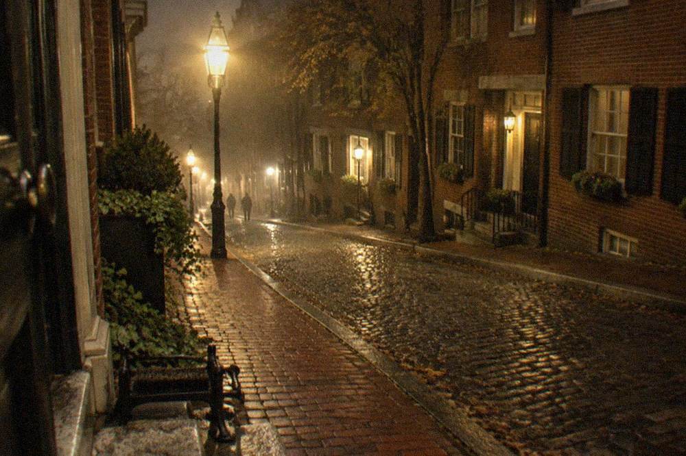 Historic brick rowhouses and a lamp-lit narrow street in Beacon Hill at night.