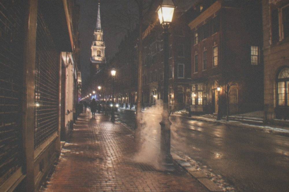 A lit historic Boston street with brick sidewalks and closed storefronts