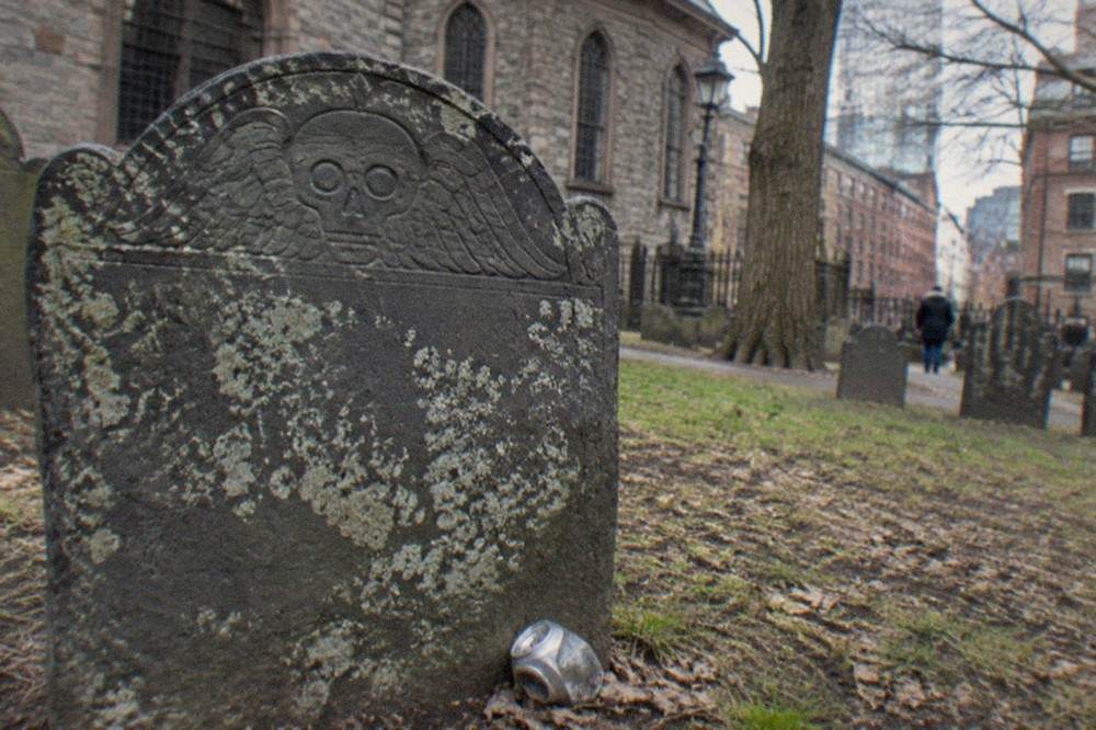 Weathered 17th-century slate headstone with carved winged skull motif in a colonial cemetery