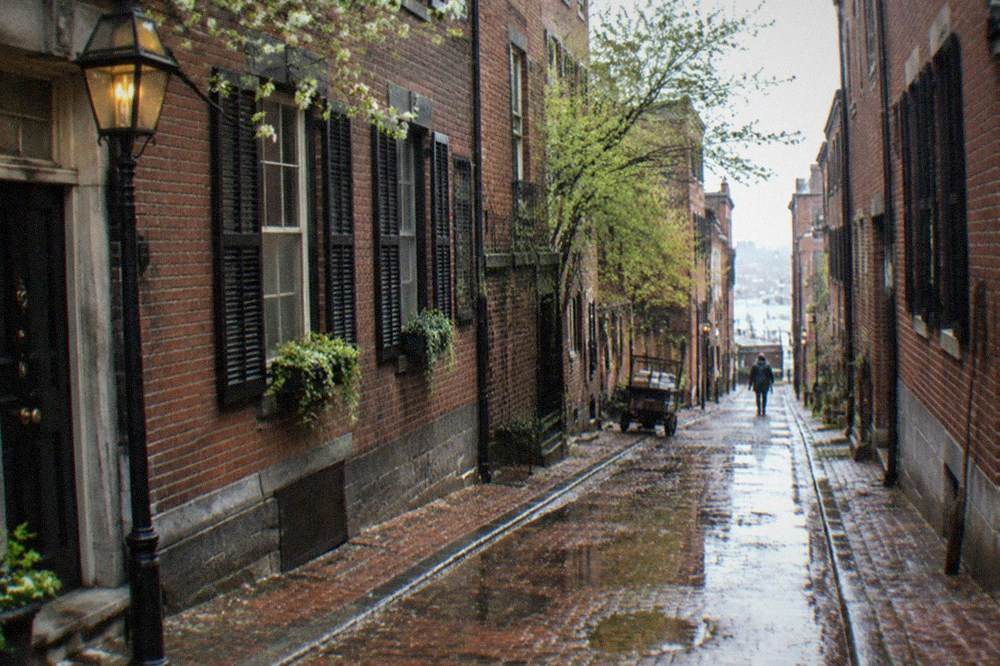 Narrow brick lane in an old New England town at twilight with gas-style lantern light