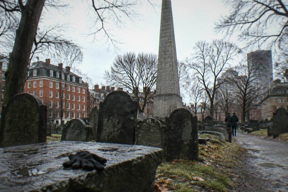 A tall stone obelisk monument rising above crowded colonial gravesites under trees