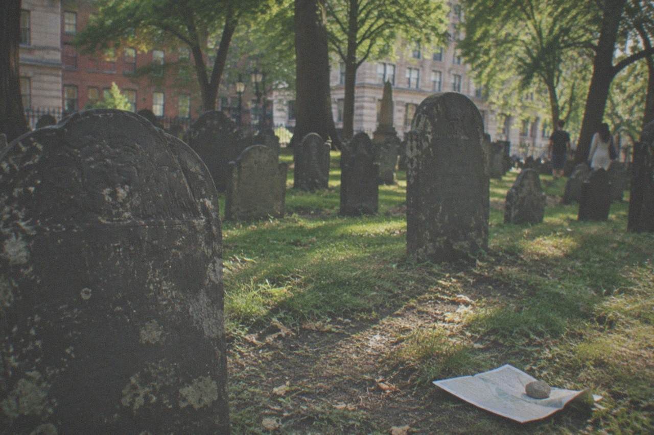 Rows of weathered colonial slate gravestones inside Granary Burying Ground with tall trees above
