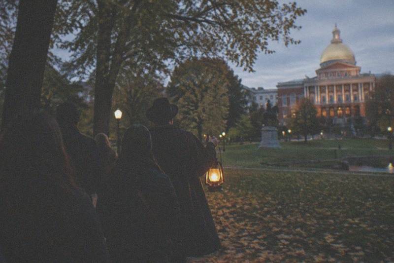 A lantern-lit ghost walk group paused on a Beacon Hill street at night