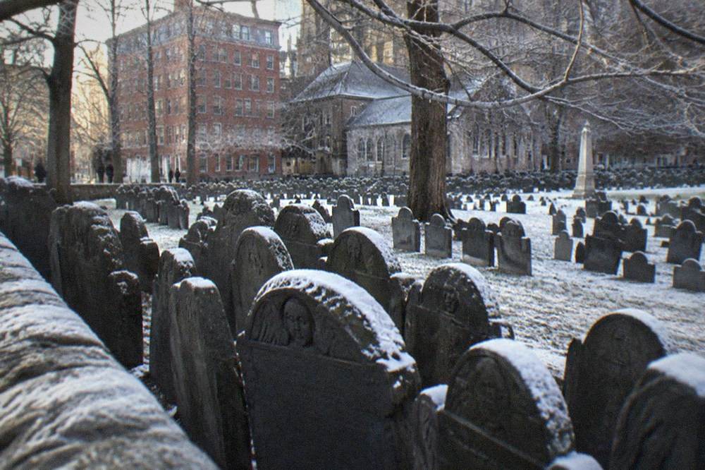 Weathered slate gravestones from the 1700s packed together in a small urban burying ground.