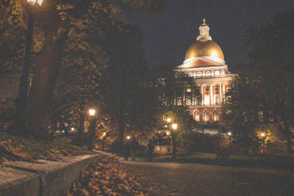 A darkened Boston street at night with the State House dome lit behind trees