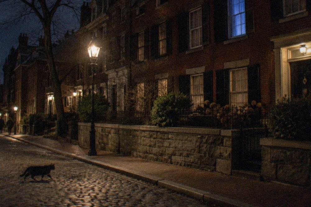 A dimly lit colonial-era Boston street with brick townhouses and a stone wall at night