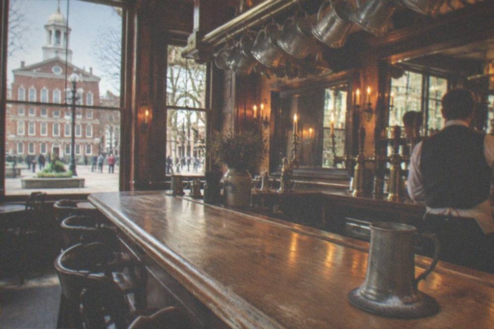 A warm-lit historic Boston tavern interior with a wooden bar and hanging glasses