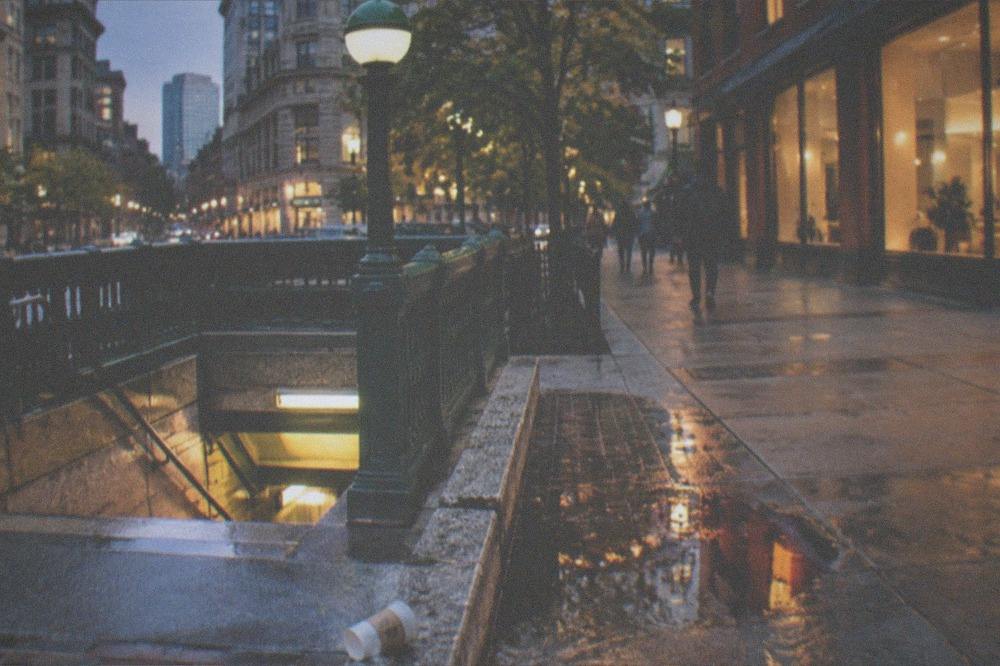 An evening street corner in downtown Boston with brick buildings and glowing shopfronts