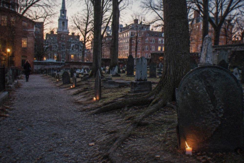 A candlelit granite gravestone path in an old Boston burying ground at dusk