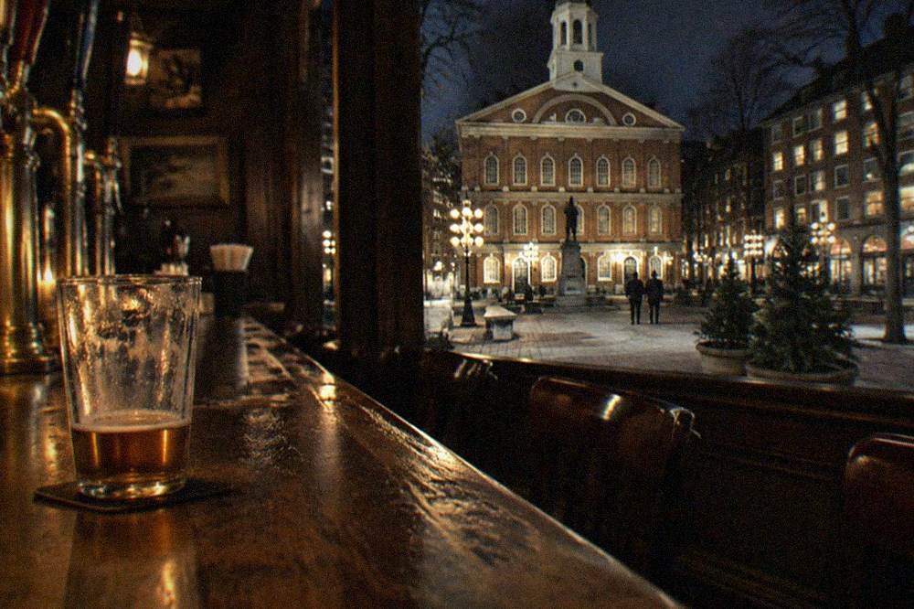 A dimly lit historic Boston tavern interior with a long wooden bar