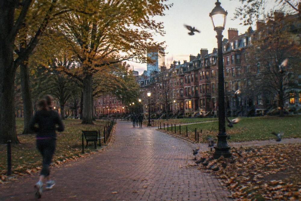 A wide brick path crossing Boston Common toward Beacon Hill row houses at twilight
