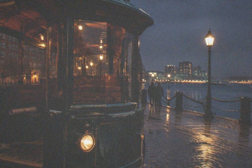 An open trolley with lit lamps parked on a Boston street near the waterfront at night