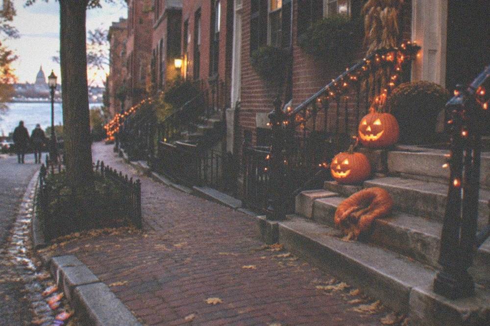 Carved pumpkins and orange lights decorating a historic Boston street in the evening