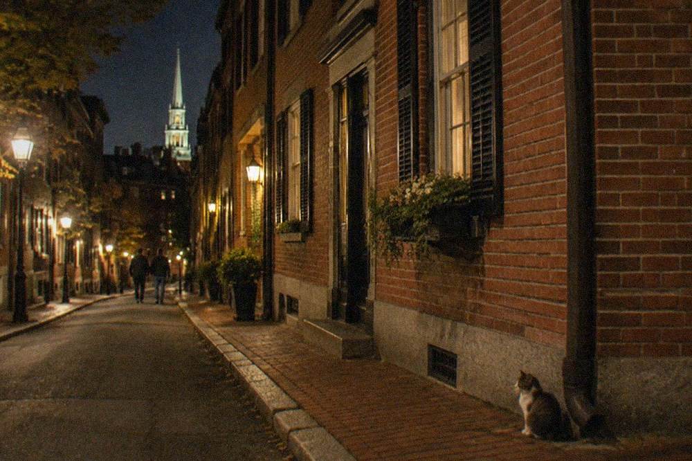 A narrow colonial-era street with brick rowhouses and warm streetlights on a Boston night tour route