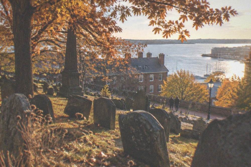 Old tilted slate gravestones beneath trees in a colonial Boston burying ground at dusk