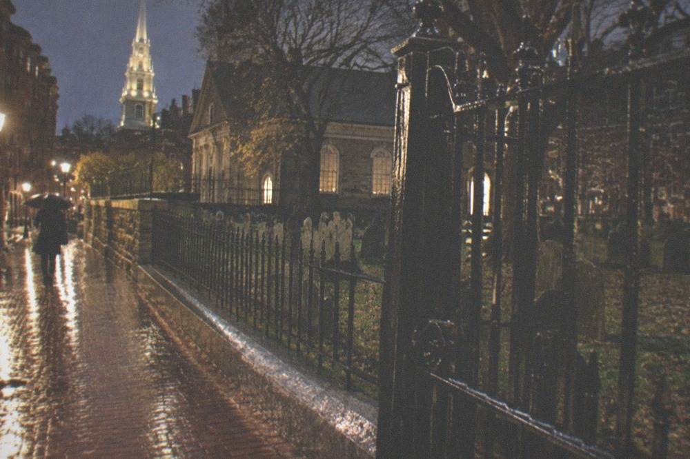 Rain-slicked brick sidewalk outside a historic Boston cemetery gate at night