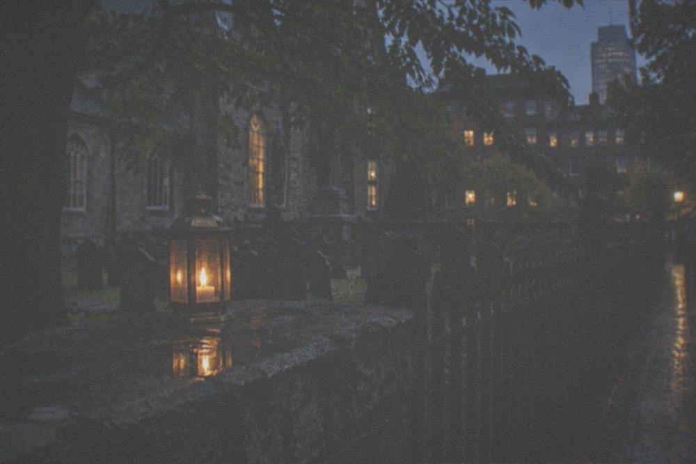 A lantern resting on a stone wall beside an old iron cemetery fence in the dark