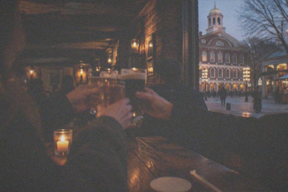 Adults raising pint glasses together at a wooden bar in a low-lit tavern