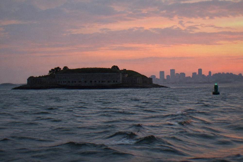 Harbor water at dusk with a dark island fort silhouette in the distance