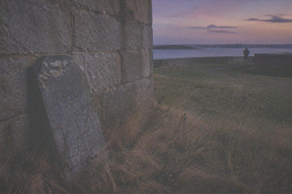 Weathered gravestone and fort wall under an evening sky near Boston harbor