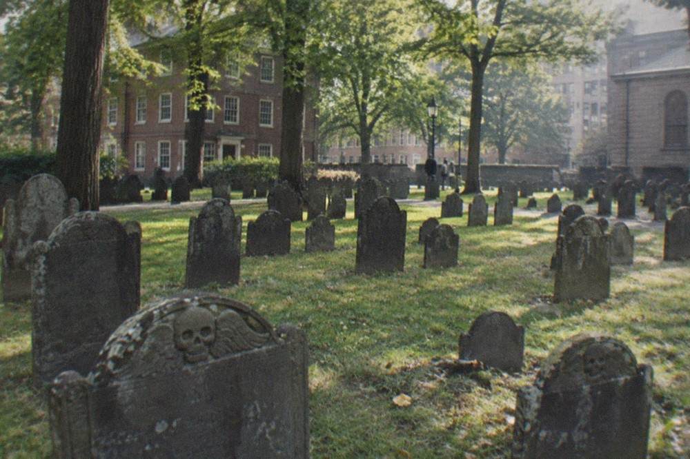 Rows of weathered colonial slate gravestones in the Granary Burying Ground with tall trees overhead