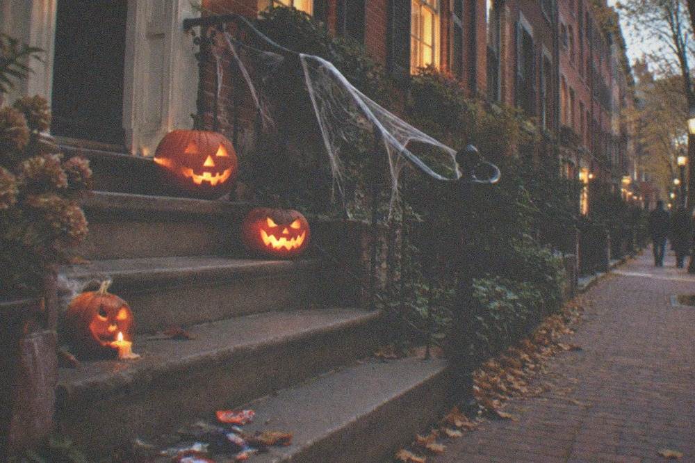 Carved jack-o-lanterns glowing on stone steps outside a decorated brick rowhouse