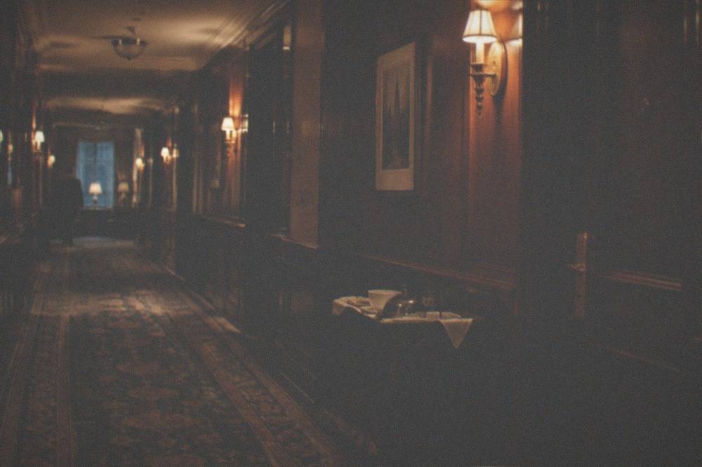 Dimly lit historic hotel corridor with patterned carpet and wall sconces