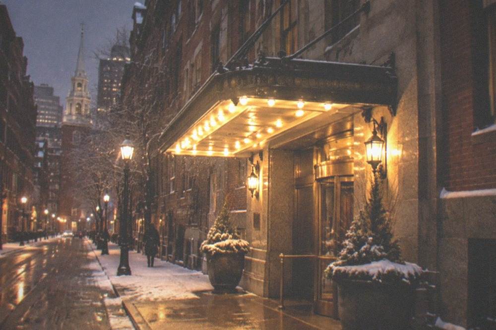 Evening street scene with a lit hotel entrance canopy on a narrow downtown Boston street