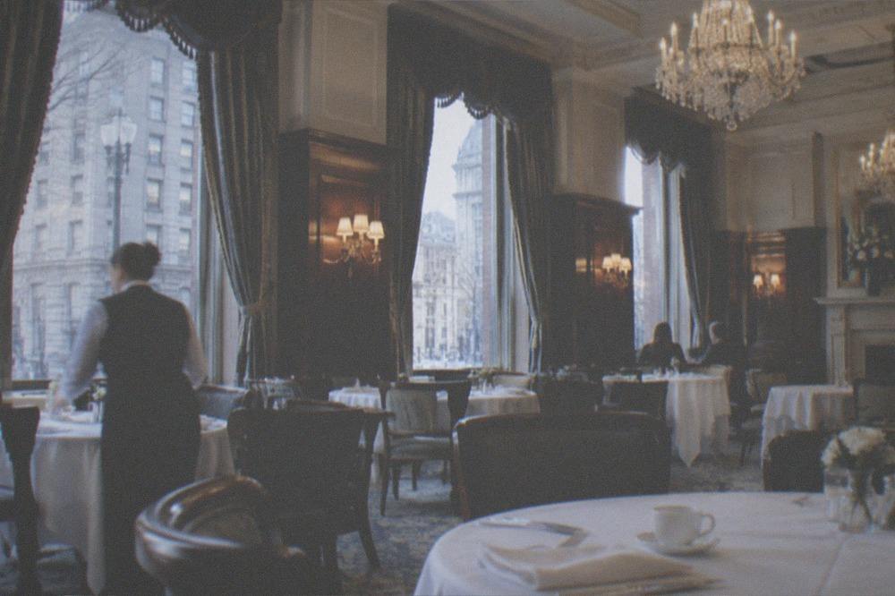 Restaurant dining room with white tablecloths, crystal chandeliers, and servers setting places