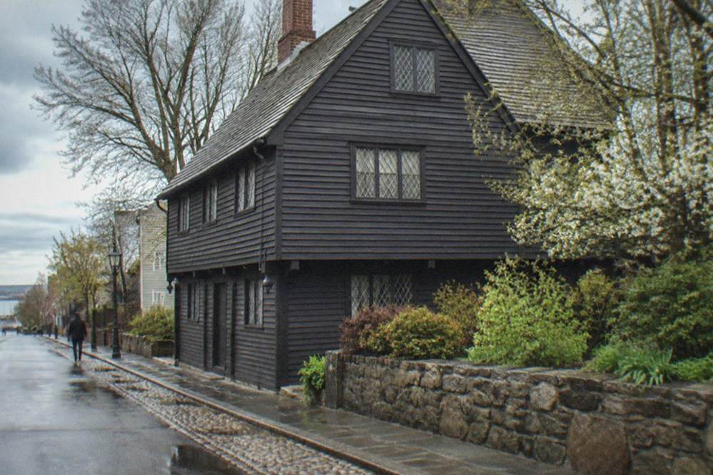 A timber-framed seventeenth-century house with dark clapboards on a narrow Salem street