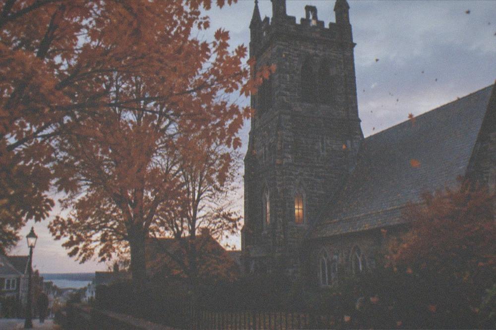 Orange and red maple leaves against a dark gray church tower in early evening
