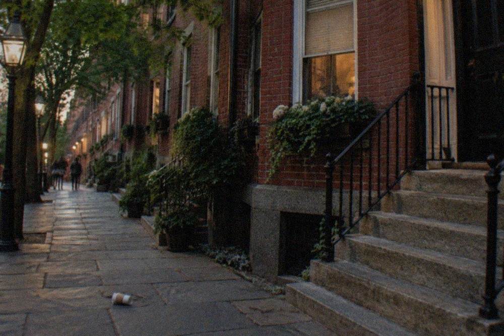 A quiet Boston street at dusk with brick townhouses and lit street lamps