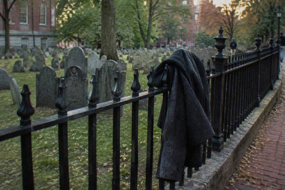 A jacket draped over a bench beside a colonial gravestone fence in evening light