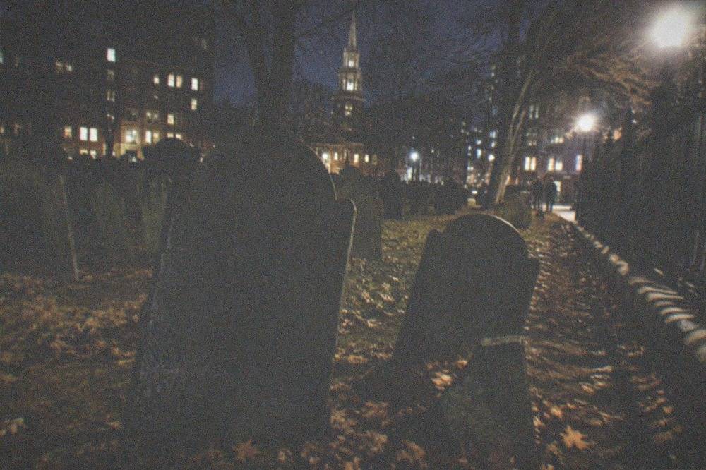 Slate gravestones in an old Boston burying ground lit by streetlight at night